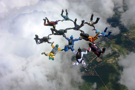 Twelve sky divers holding hands in a two interlocking circles of cooperation and teamwork