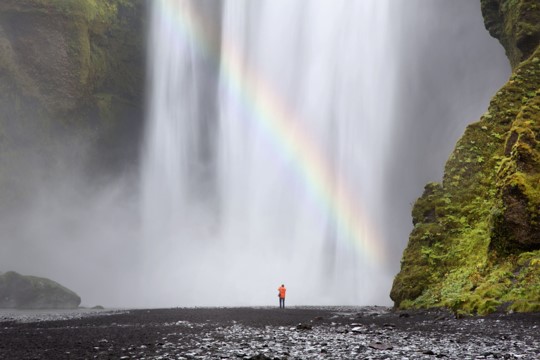 Person standing underneath a waterfall with a rainbow of hope