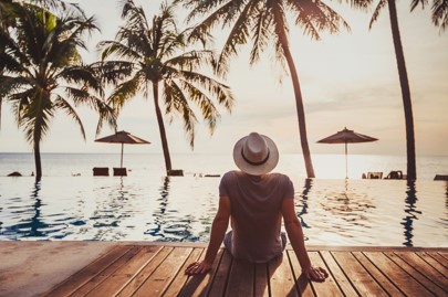 Person seated on the edge of an infinity pool gazing out past the palm trees to the ocean