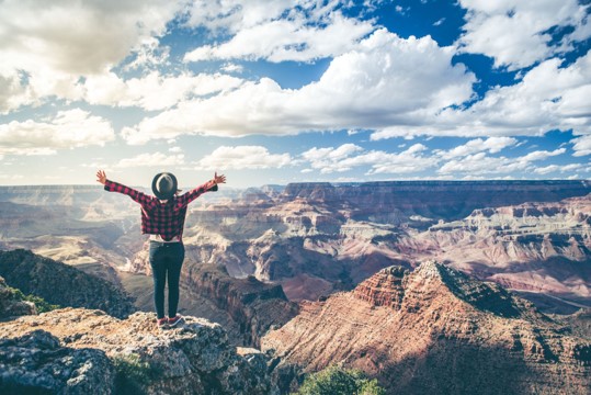 Hiker standing along cliff overlooking the Grand Canyon with their arms flung wide in jubilation