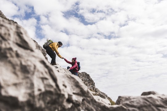 Two people climbing a mountain together with outstretched hands helping each other up